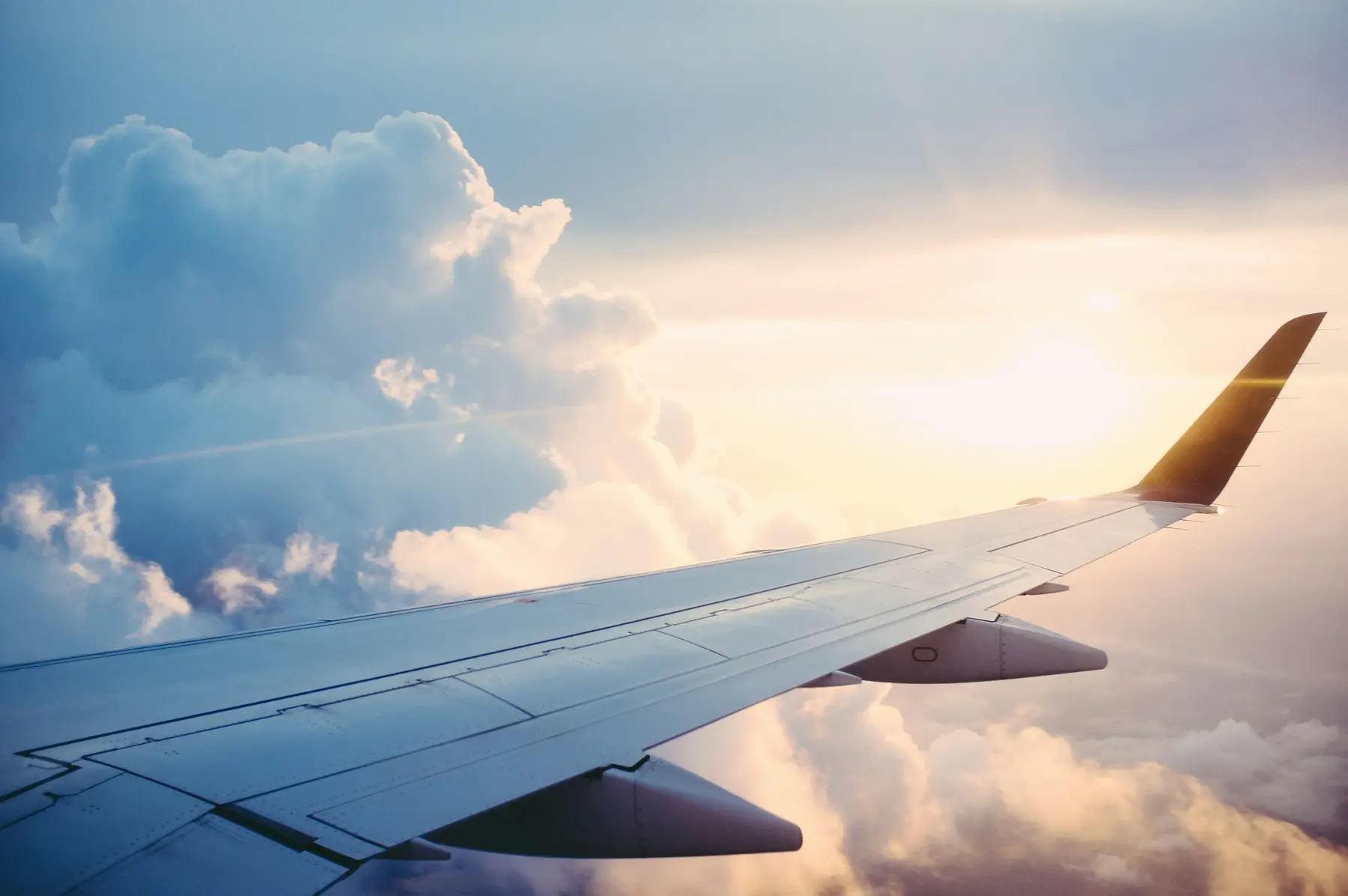 Asa de um avião sobre nuvens volumosas iluminadas pelo sol nascente